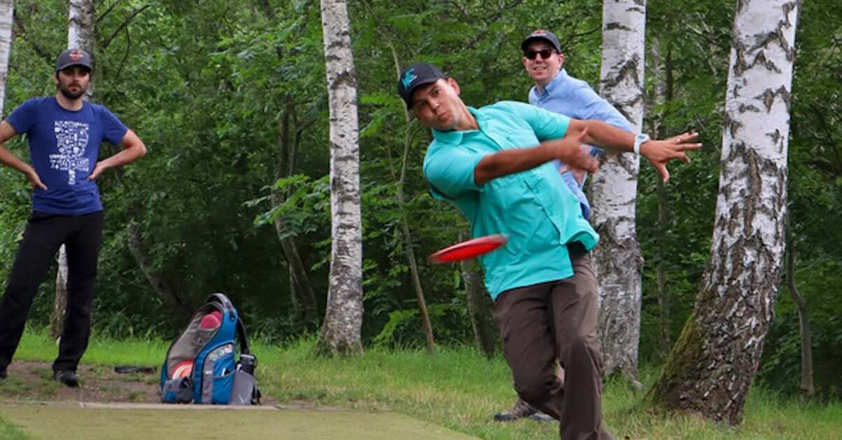 One disc golfer throws a forehand while two others look on