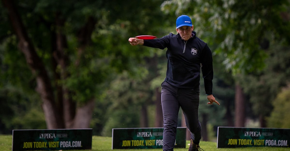 A woman in a blue hat, jacket, and outdoor pants throwing a disc golf disc