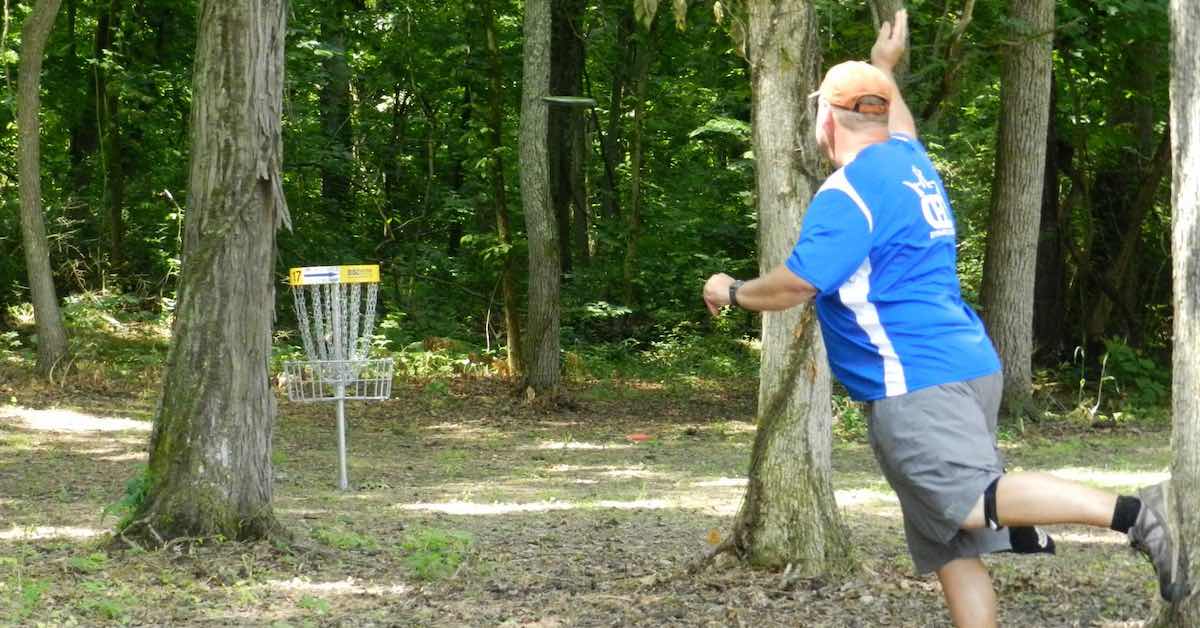 Man putts a disc to a basket on a wooded green