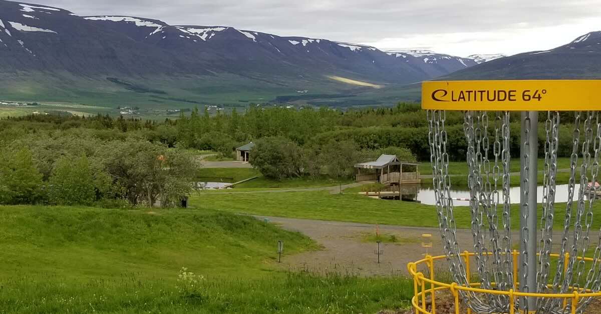 A yellow disc golf basket in an open grassy area with a view of snow-capped mountains beyond
