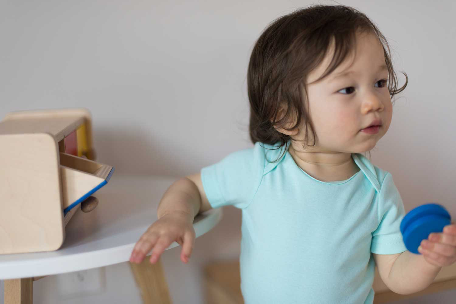 baby wearing a blue baby suit holding a wooden blue disc