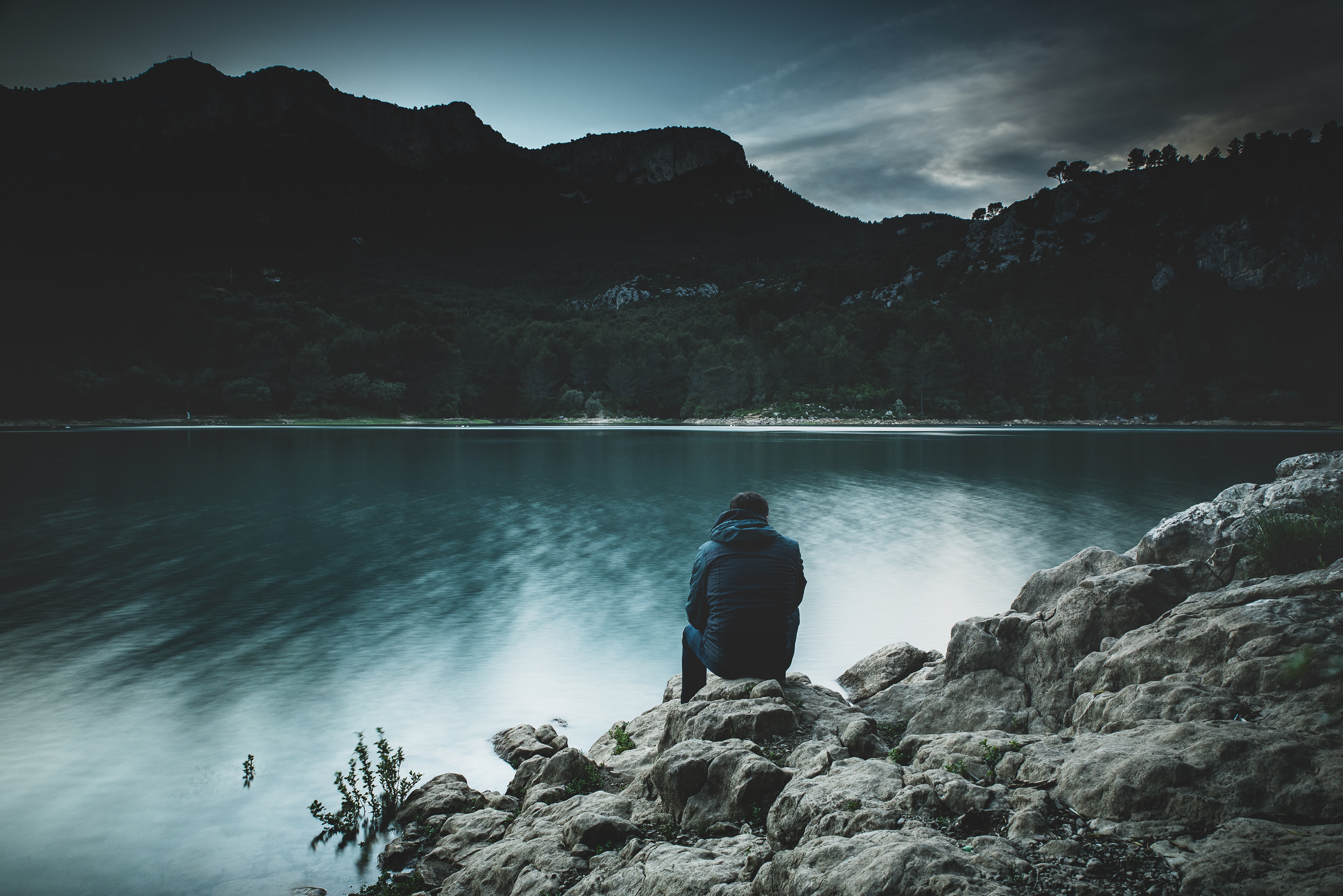 Man sitting at lake near mountains