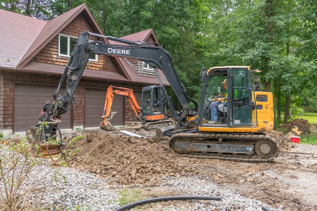 John Deere and Kubota mini excavators working on a driveway in front of a house