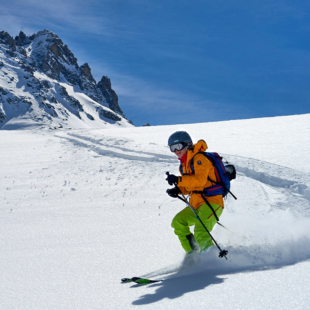 Person skiing down a hill under a blue sky.