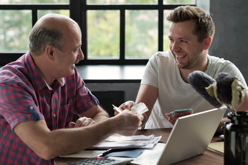 two men smiling and exchanging cash