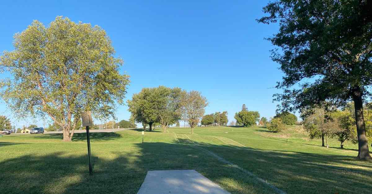 A concrete disc golf tee pad in mown park landscape with scattered mature trees