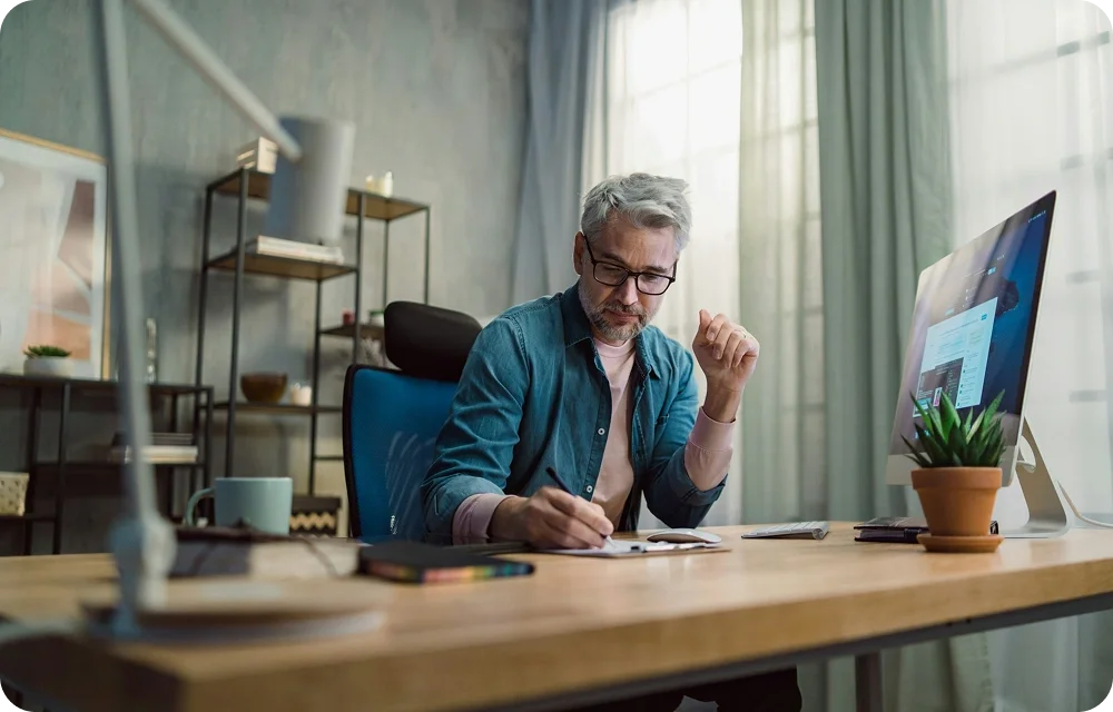 Man writing on a notebook, while working in front of a computer