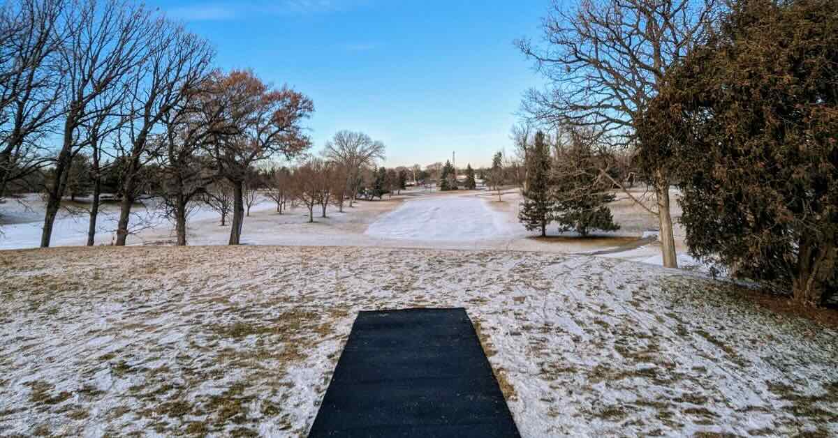 A black disc golf tee in a lightly snowy golf course setting