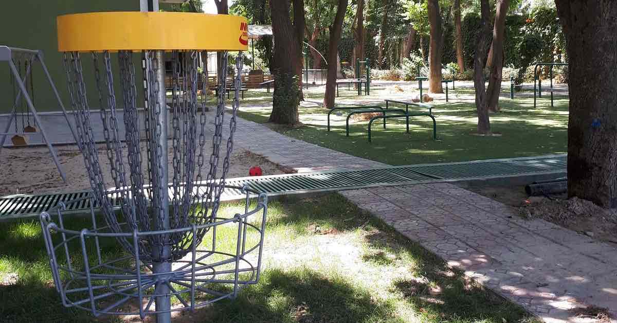 A disc golf basket near a school playground