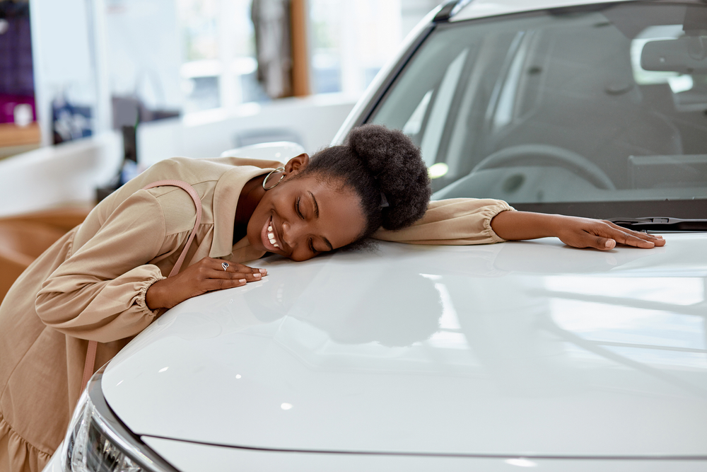 Happy lady hugging her new white car in the dealership