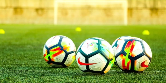 Three soccer balls lay on a field of green grass.