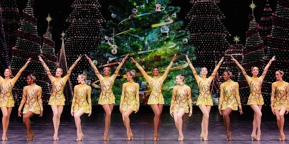 A group of performers on stage in holiday outfits.