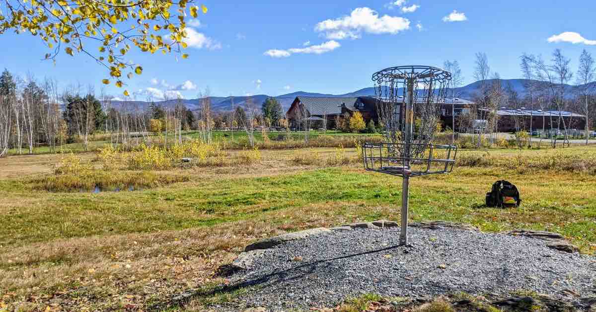 Disc golf basket in open grassy area with rolling mountains in the distance