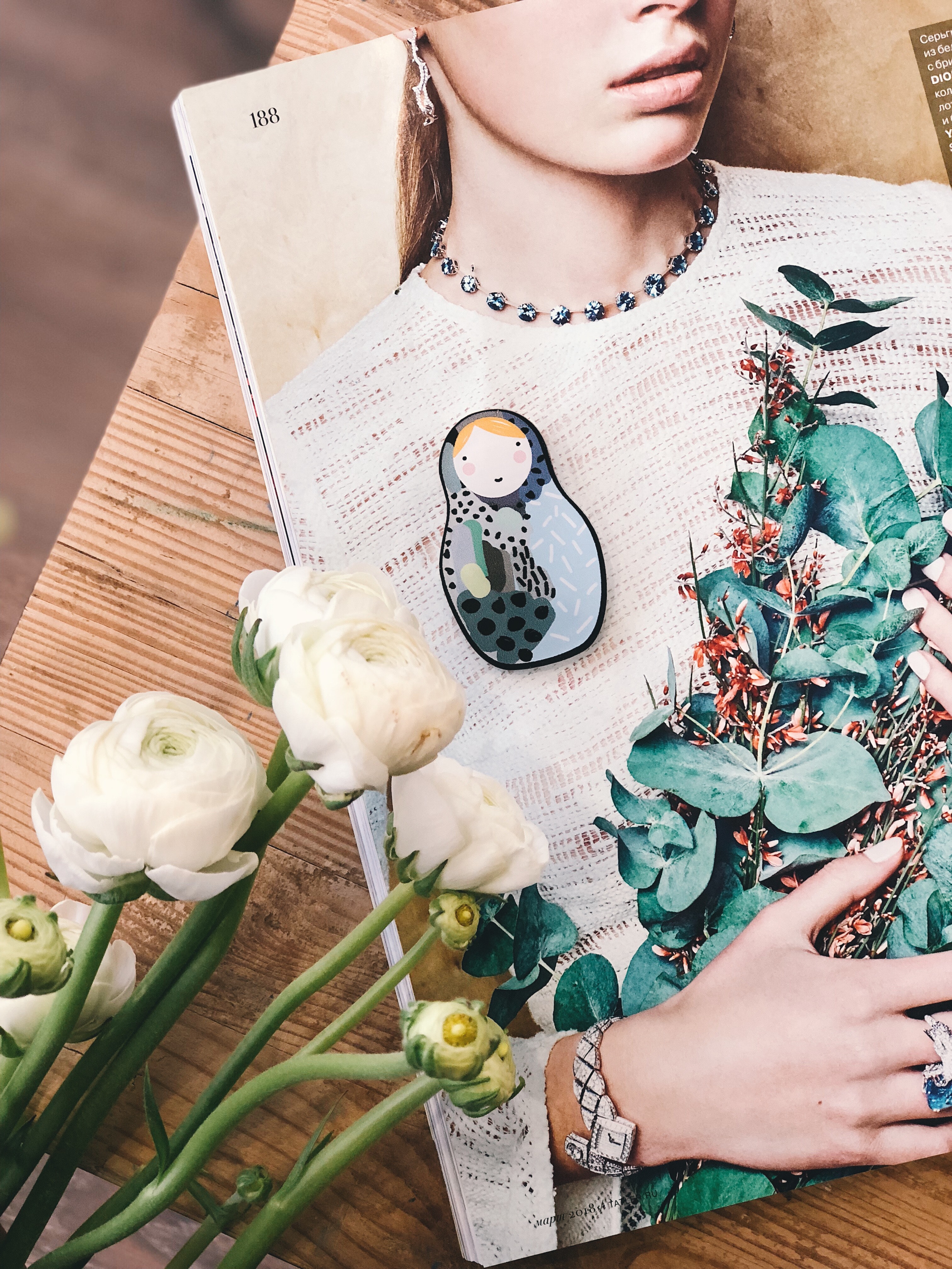 open page of a magazine featuring a women in jewelry holding a green plant with roses on the table