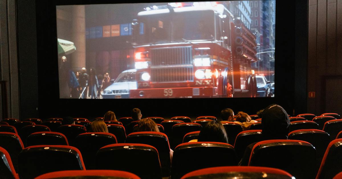 A movie theatre with an audience, the screen showing a scene involving a fire truck.