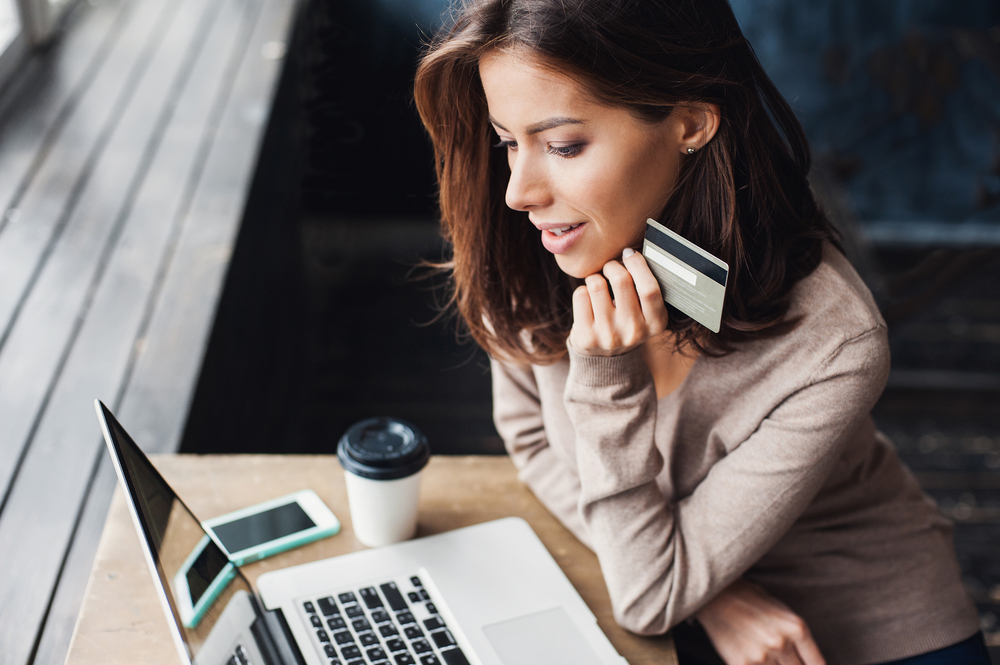 Young woman on her laptop in a coffee shop holding a credit card