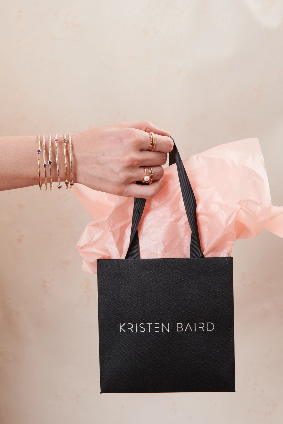 hand holding a Kristen Baird shopping bag with lots of jewelry on it 