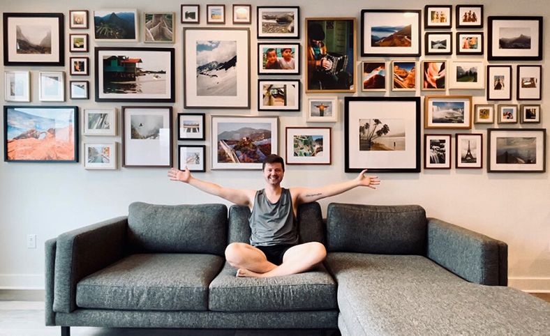 gallery wall of travel photos with man on couch