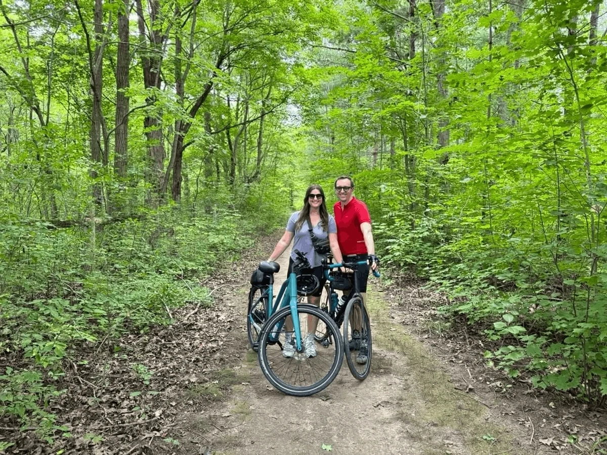 Travel bloggers Christopher and Bri pose with bikes in a forest in Waterloo, Ontario, Canada.