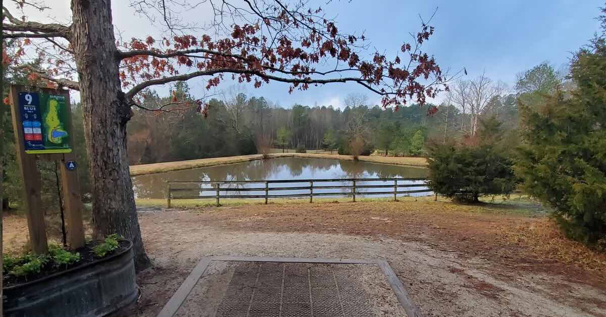 A disc golf tee pad leads to a fairway with a pond in it