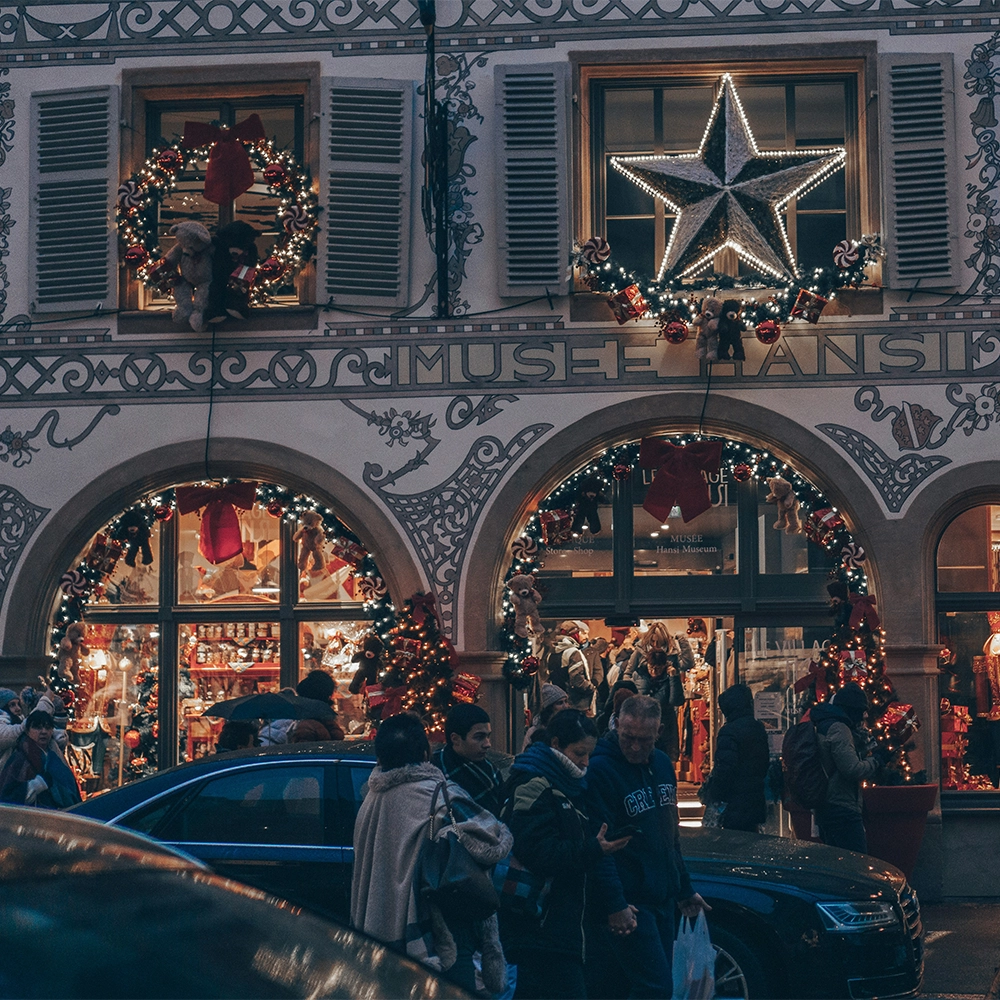 Busy street in front of a building filled with Christmas decor in Colmar, France.