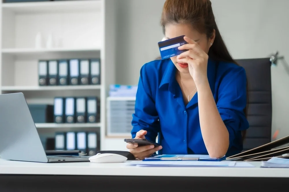 Woman looking at her phone and holding up a credit card
