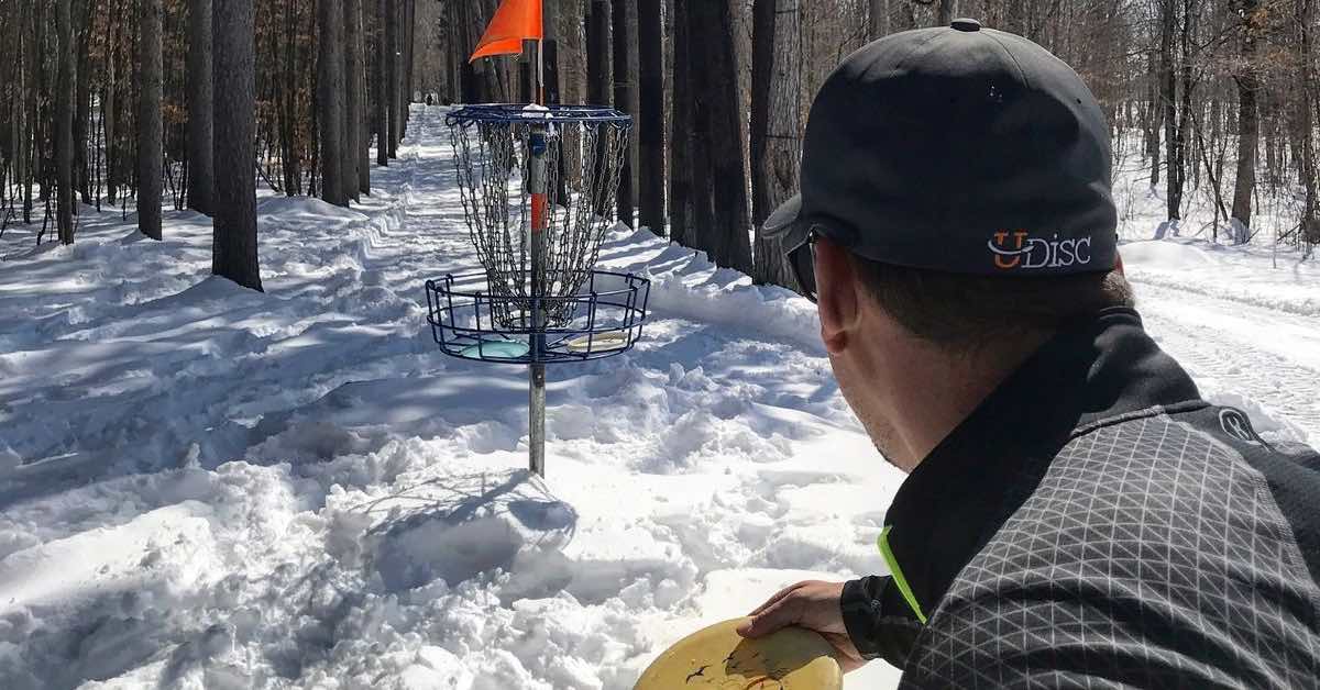 Close up of back of man's head putting at a disc golf basket on a snowy course