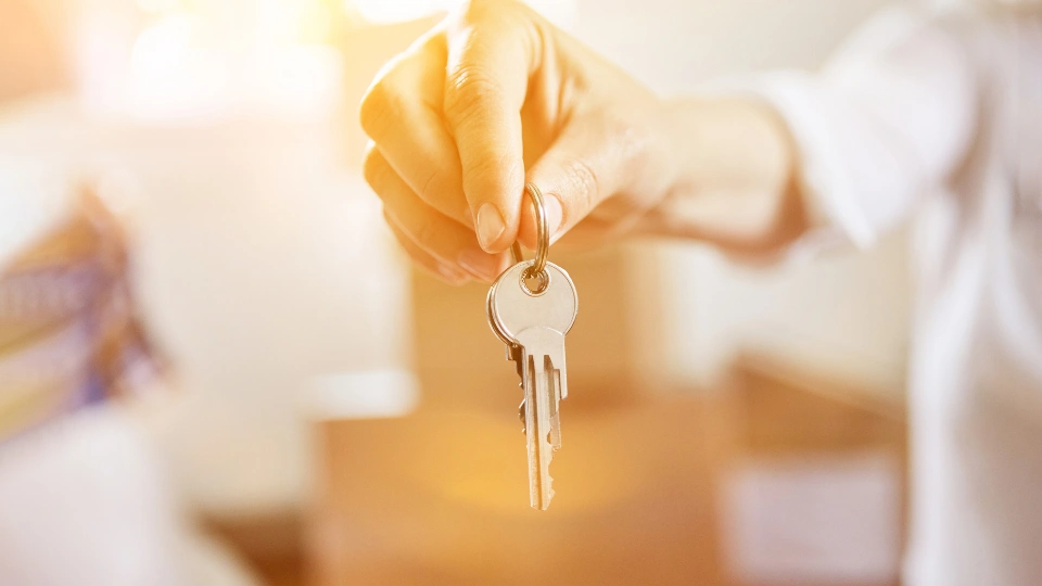 Hand of landlord with a key at a house