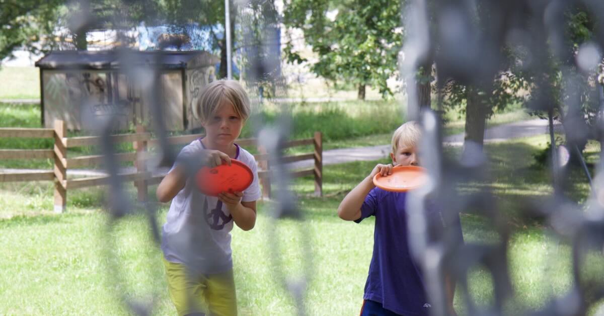 Two kids putting at disc golf basket seen through basket chains