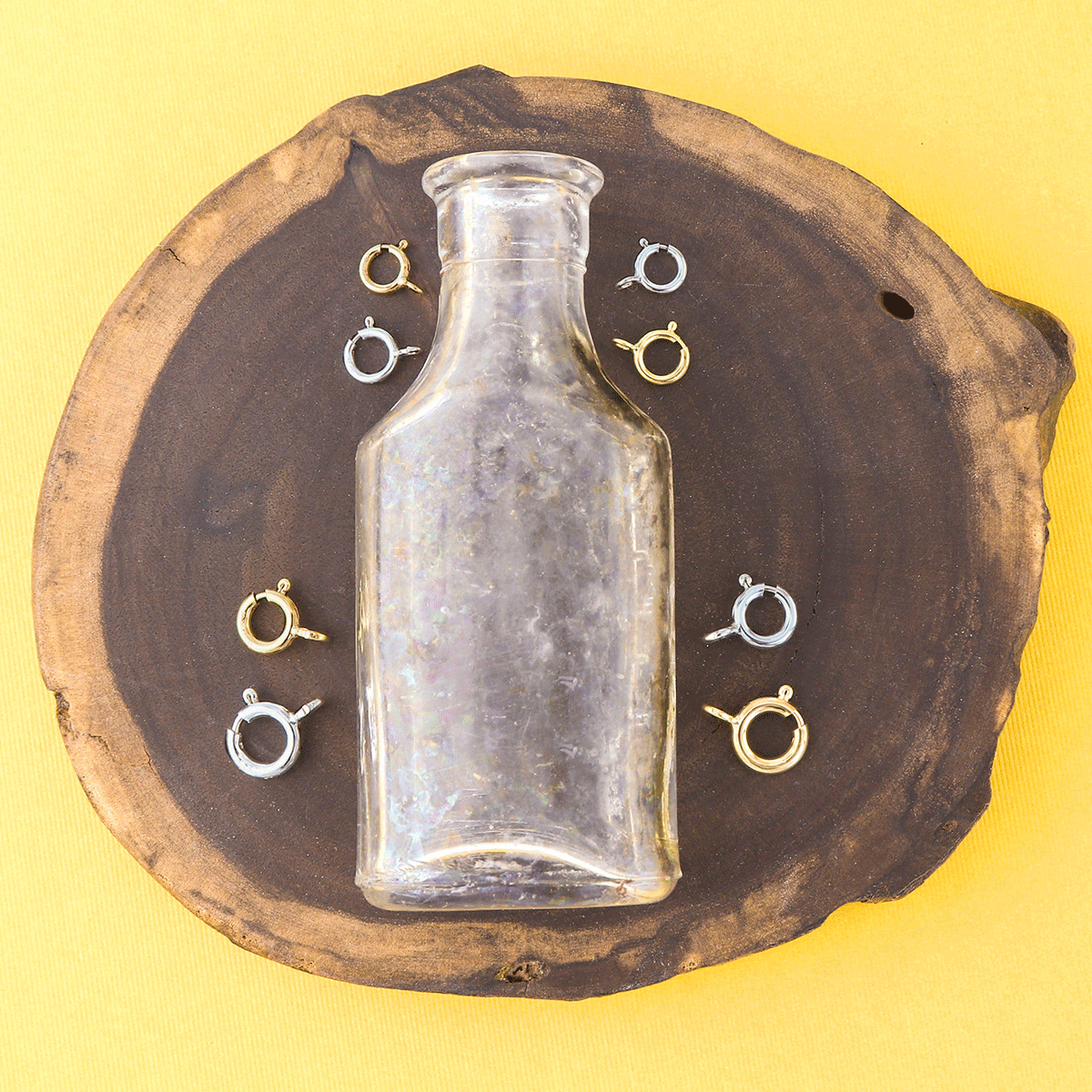 glass bottle on a piece of wood surrounded by silver and gold spring ring clasps of different sizes