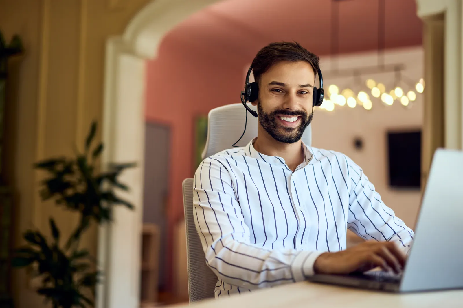 Smiling man wearing a headset while using a laptop at home