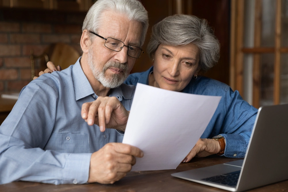 Older couple looking over a document with their laptop open