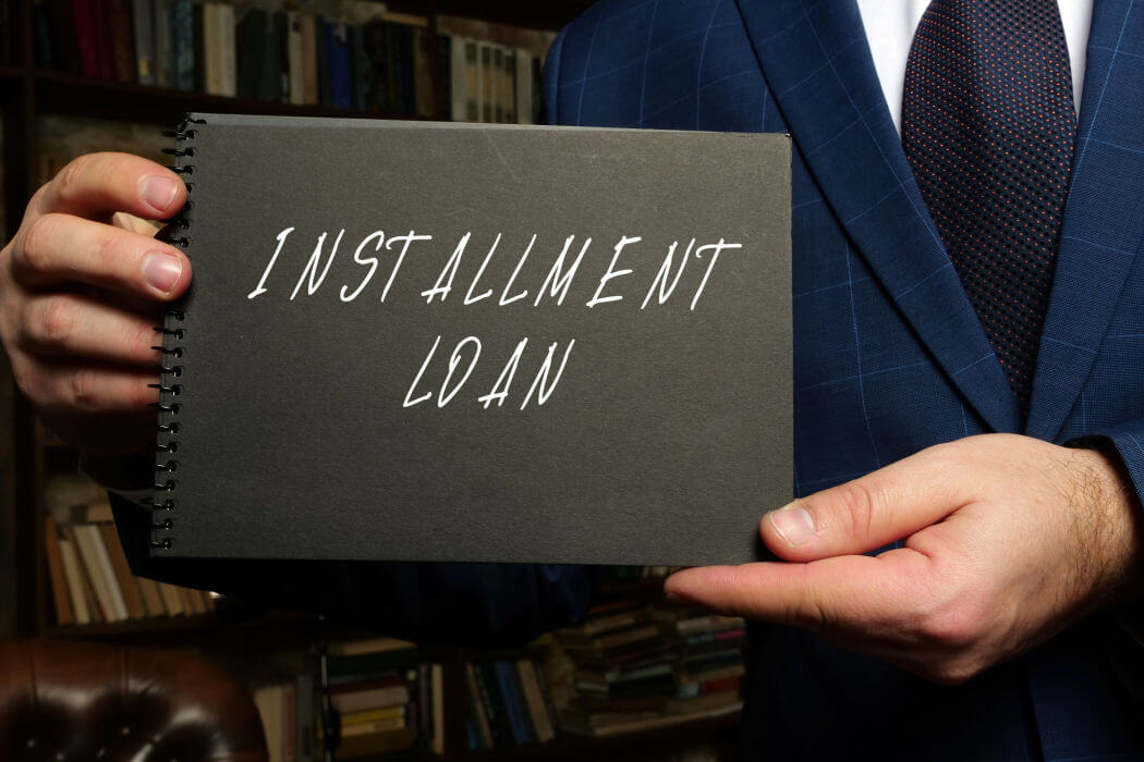 A white man holds a black notebook with installment loan written on the cover.