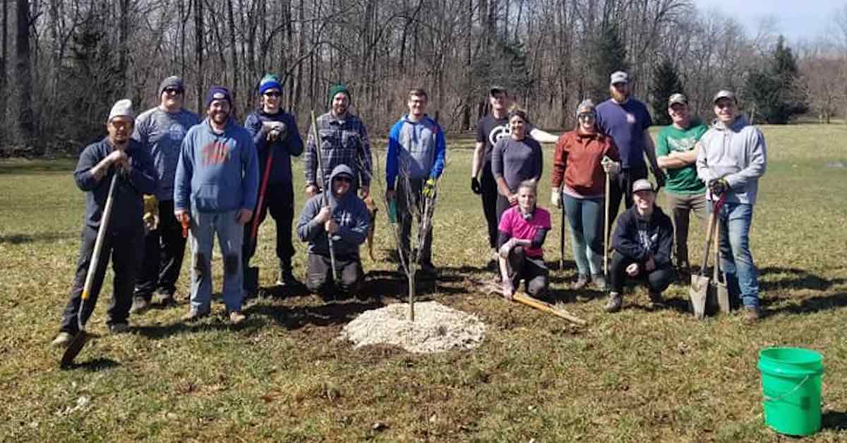  A group with shovels stand around a newly planted tree