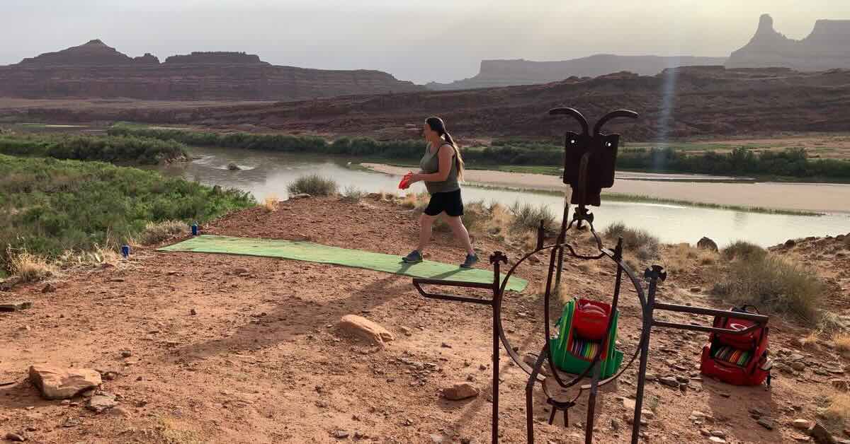 A woman on a turf disc golf tee pad in a red rock desert preparing throw a disc golf shot