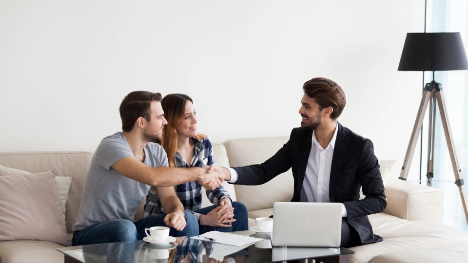 real estate agent shaking hands with a couple sitting on a couch