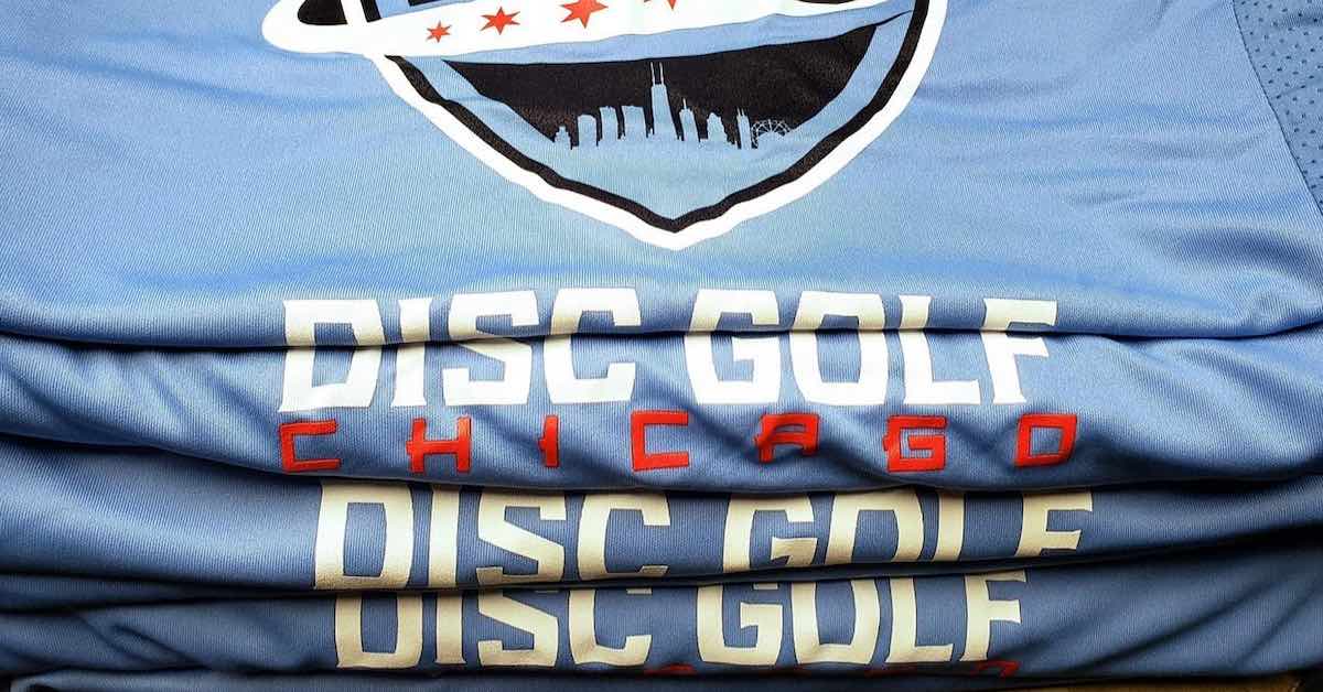 A stack of folded blue tee shirts that say Disc Golf Chicago