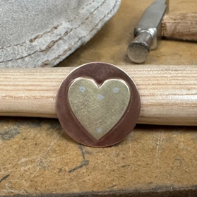 brass heart flush riveted to a copper circle with 4 silver rivets