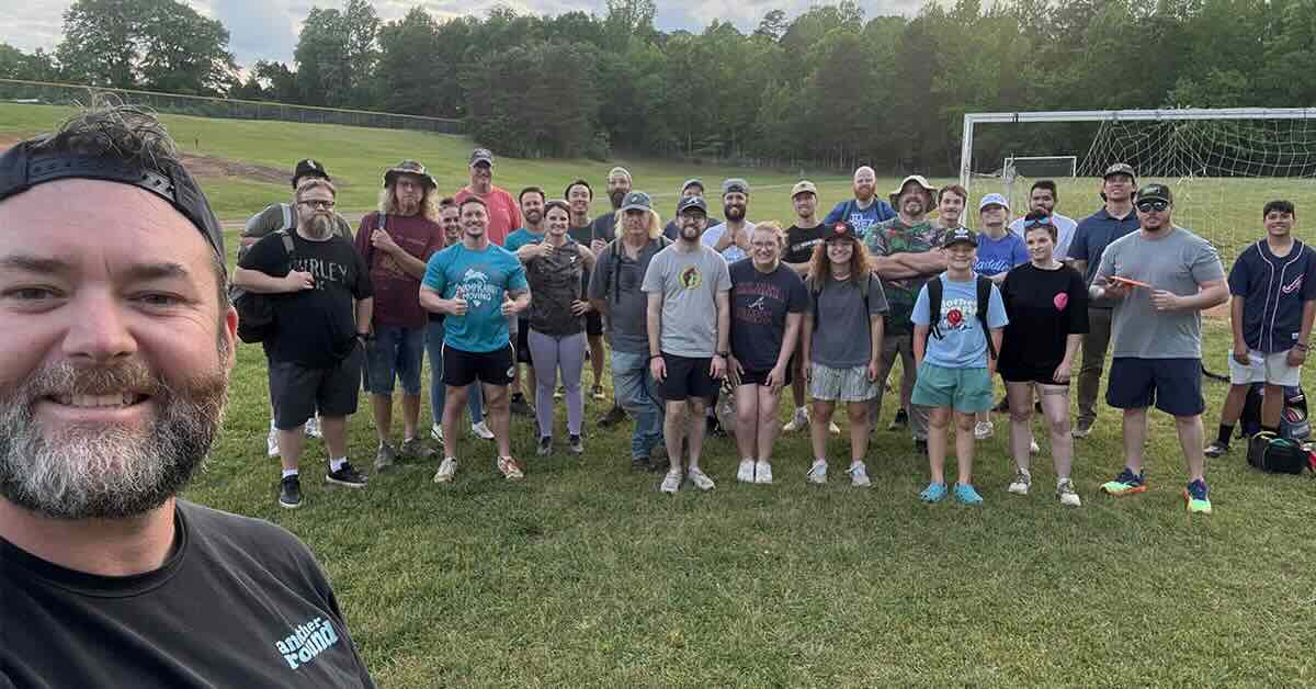 A group ready to play disc golf poses for a photo in a soccer field