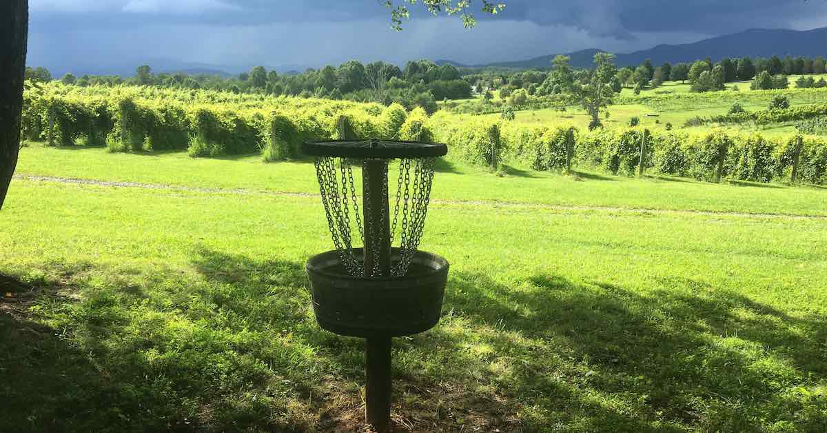A disc golf target made with a half wine barrel as a basket. Vineyards and mountains with storm clouds in background