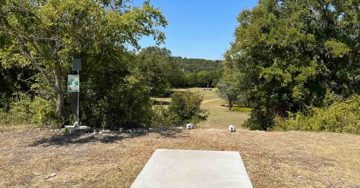 A concrete disc golf tee pad on an area elevated above a fairway below. Baske in distance