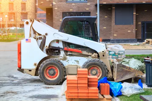 Skid steer moving bags next to a pallet