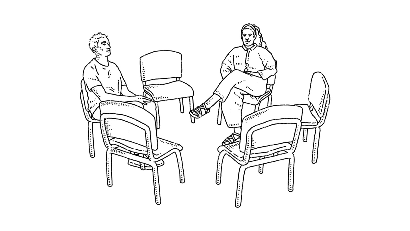 A community support group of two people sitting in a circle of chairs. Four chairs are empty.