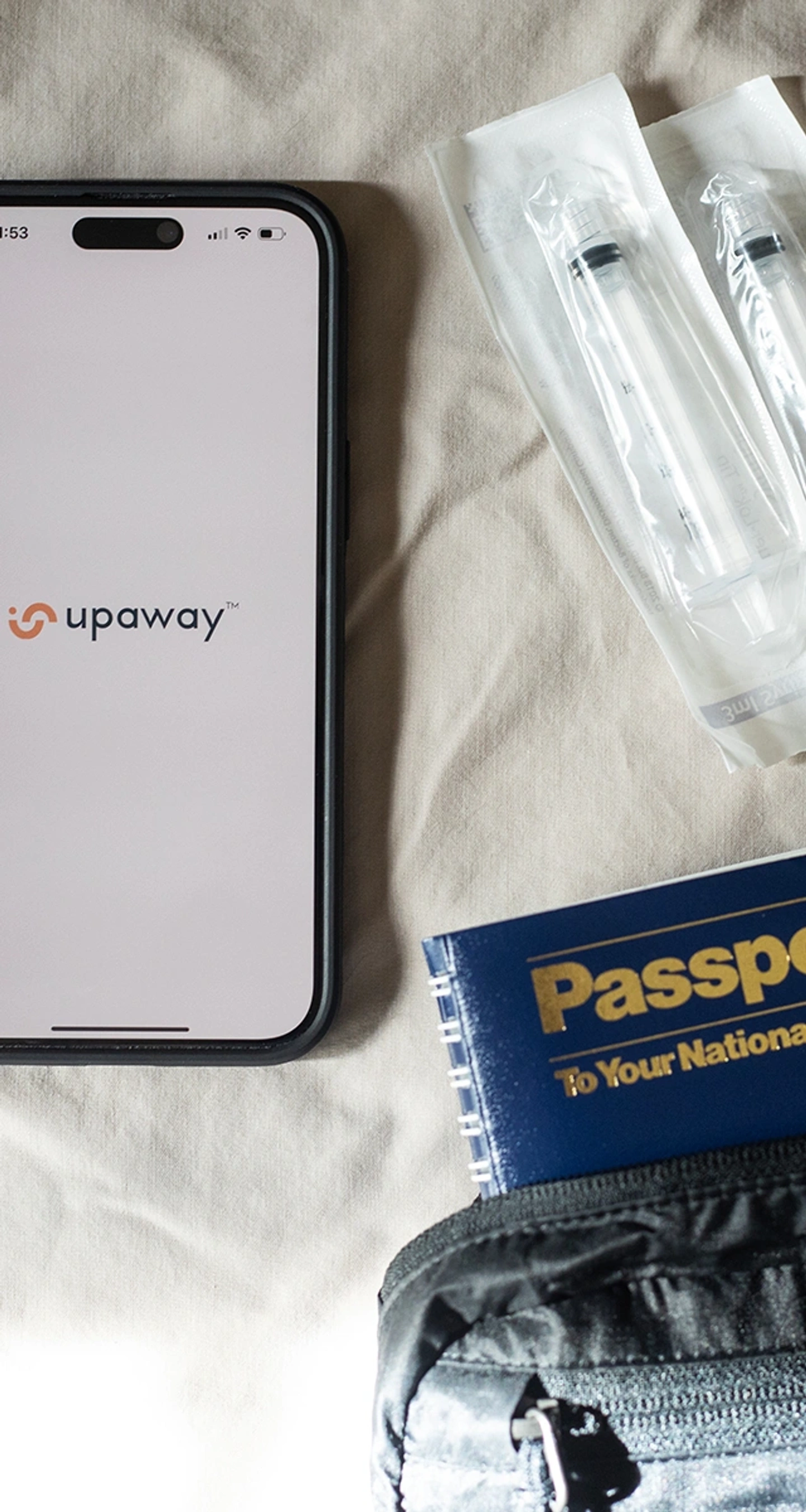 A smartphone with the Upaway app open, passport, syringes, needles, and band aids are spread out on a bed sheet.