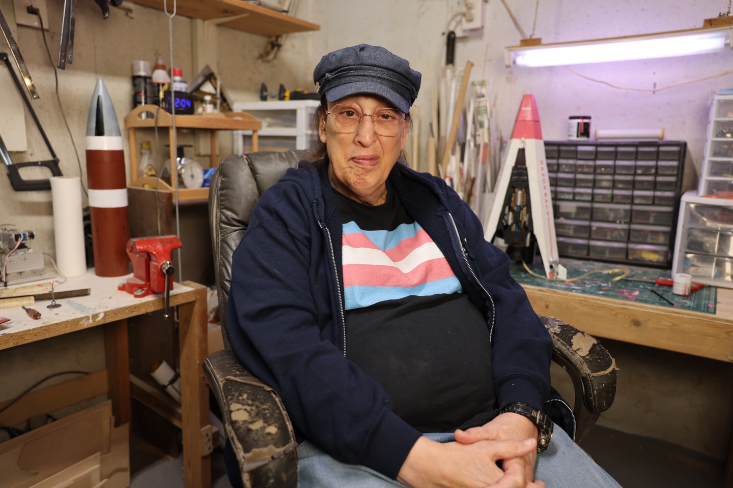 Monica Helms sitting in a chair wearing a shirt that has the trans flag on it