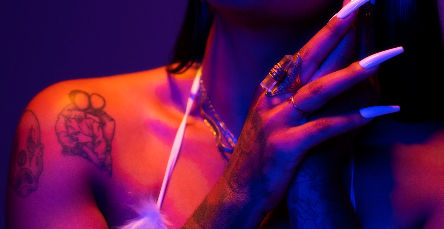 A tattooed hand with long nails and rings, and a tattooed shoulder.