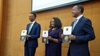 Three people dressed smartly line up holding awards smiling