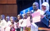 A group of interns stand on stage in a row holding a quote on a paper.