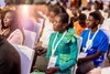 Woman in a bright green dress with a lanyard around her neck sitting in a crowd at a conference