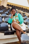 A young woman wearing a bright teal shirt and white skirt sitting in the seats of an empty stadium IDPD 2025